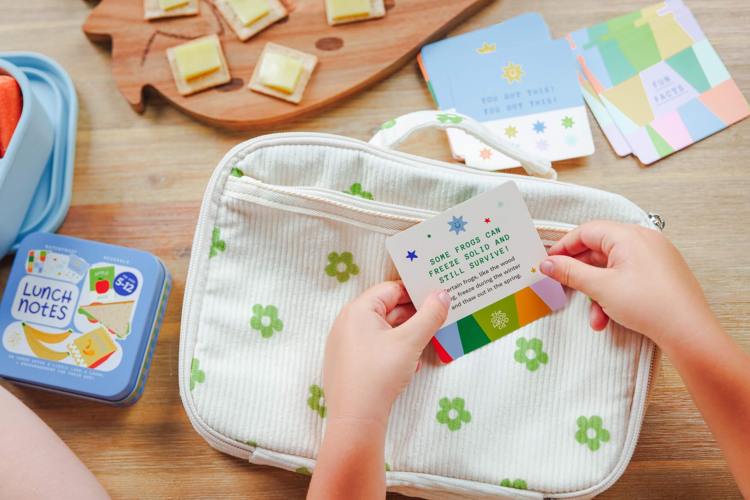 Person holding a lunch box with educational cards on a wooden surface